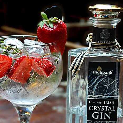 round glass with gin  ice and strawberries beside bottle of Kilkenny Crystal Gin