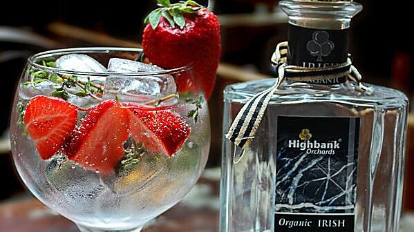 round glass with gin  ice and strawberries beside bottle of Kilkenny Crystal Gin