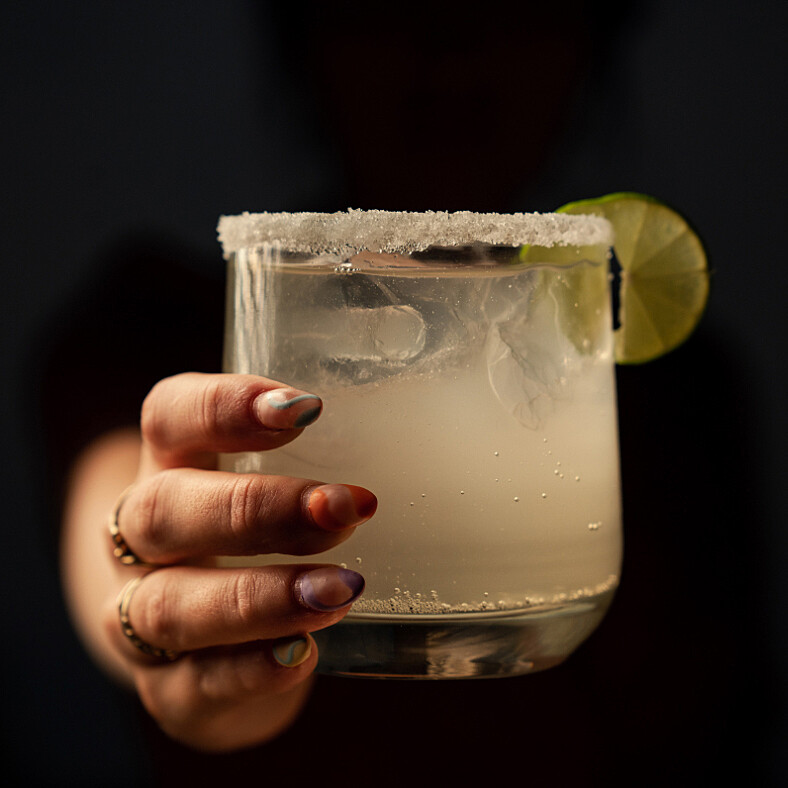 hand holding an apple cider margarita with frosted lip glass and slice of lime