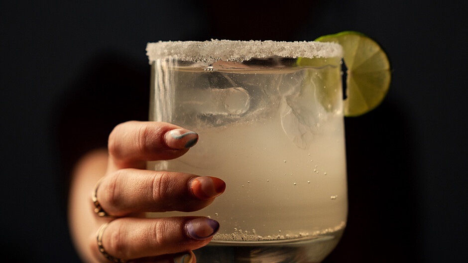 hand holding an apple cider margarita with frosted lip glass and slice of lime