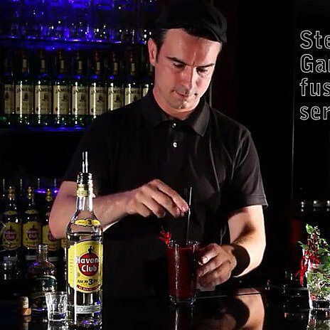 Mixologist at a bar surrounded by glasses and bottles preparing a drink