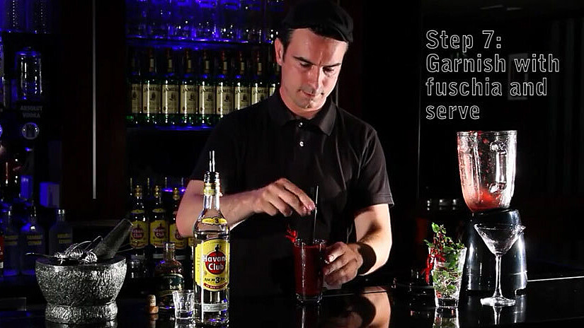 Mixologist at a bar surrounded by glasses and bottles preparing a drink