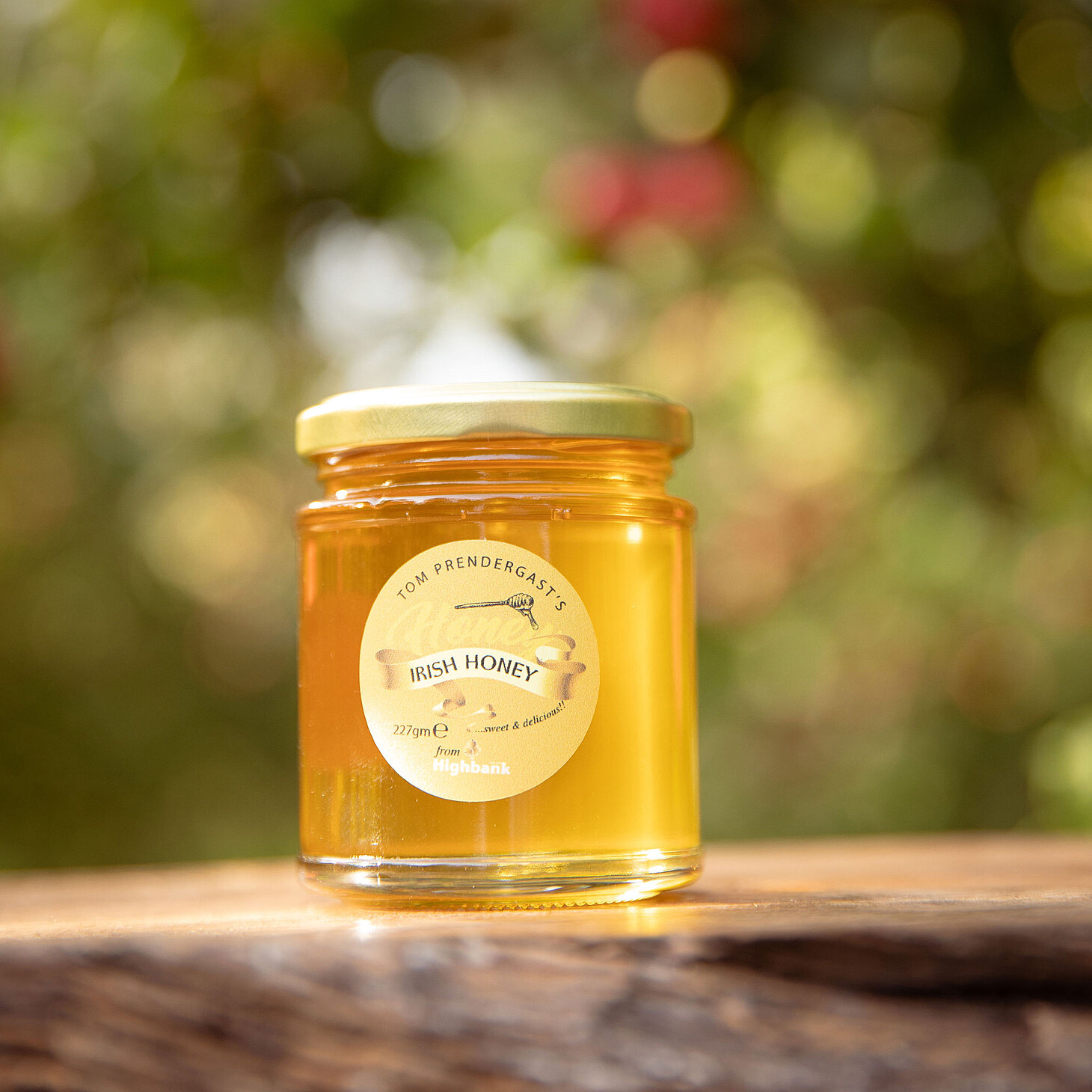 Jar of Highbank Honey with gold lid on wood beside an apple with leaves. yellow circular label