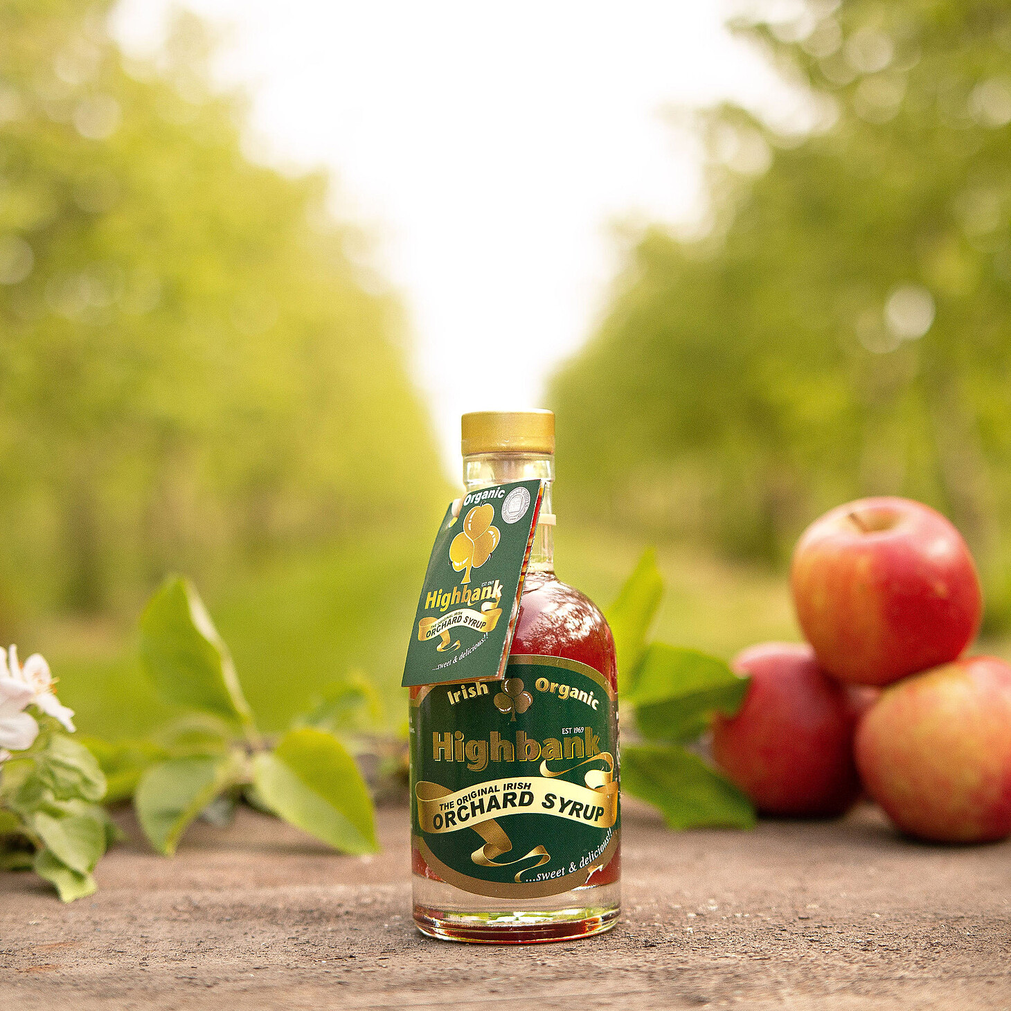200ml bottle of orchard syrup on wood beside an apple with leaves. Green label with yellow sash