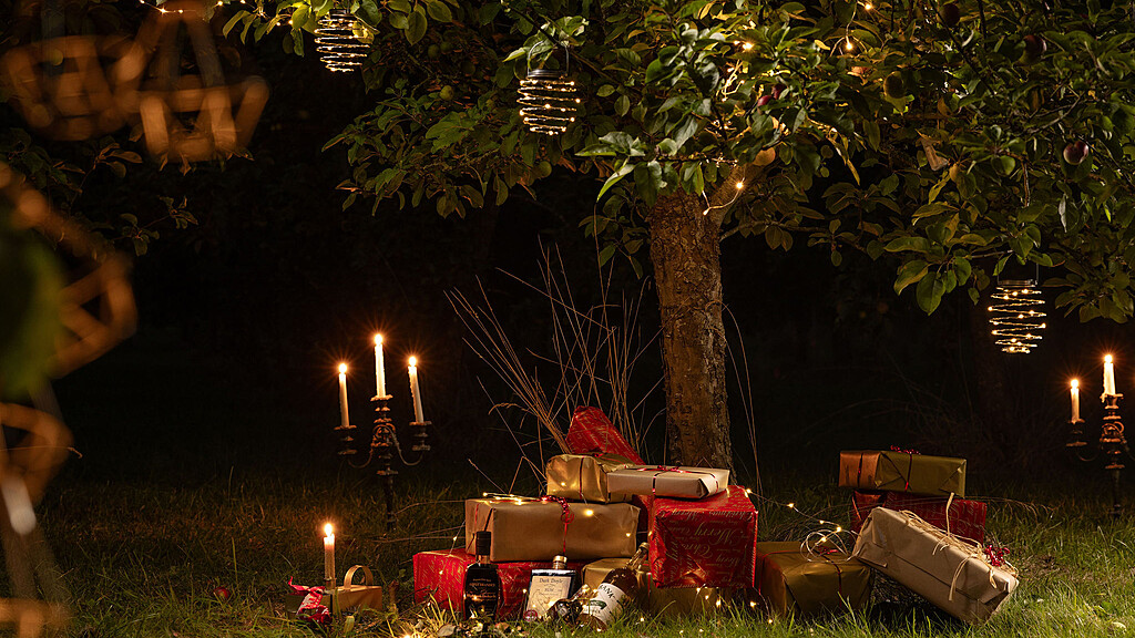 Christmas parcels and presents with lit candelabra under apple tree instead of a Christmas tree at night