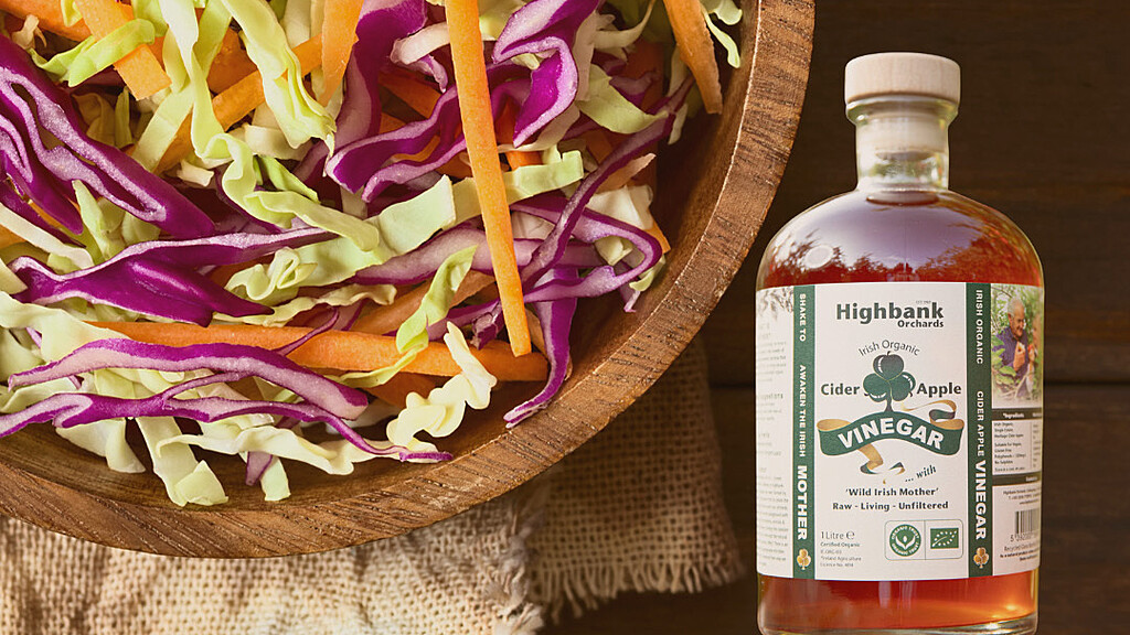 Wooden Bowl of Tangy coleslaw next to bottle of Highbank Apple cider Vinegar