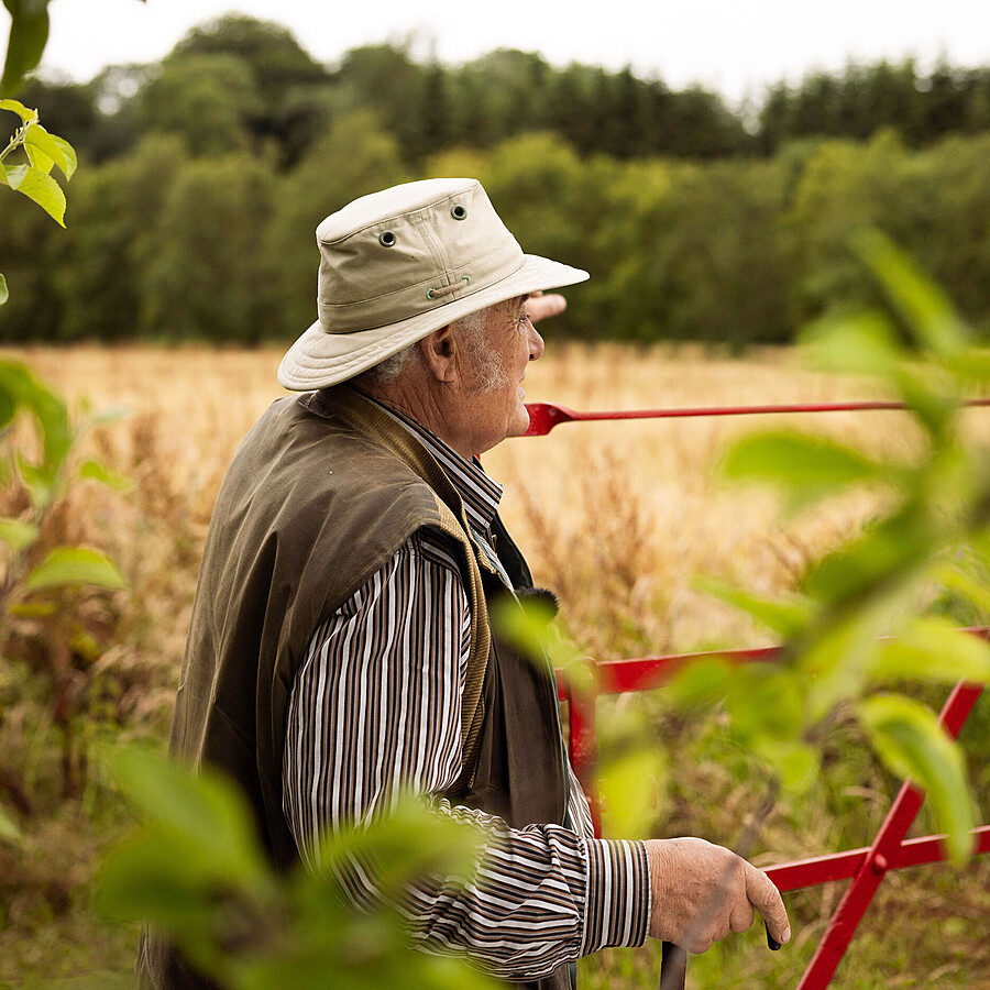 Rod with hat on looking over red Gate to a lovely field of yellow oats