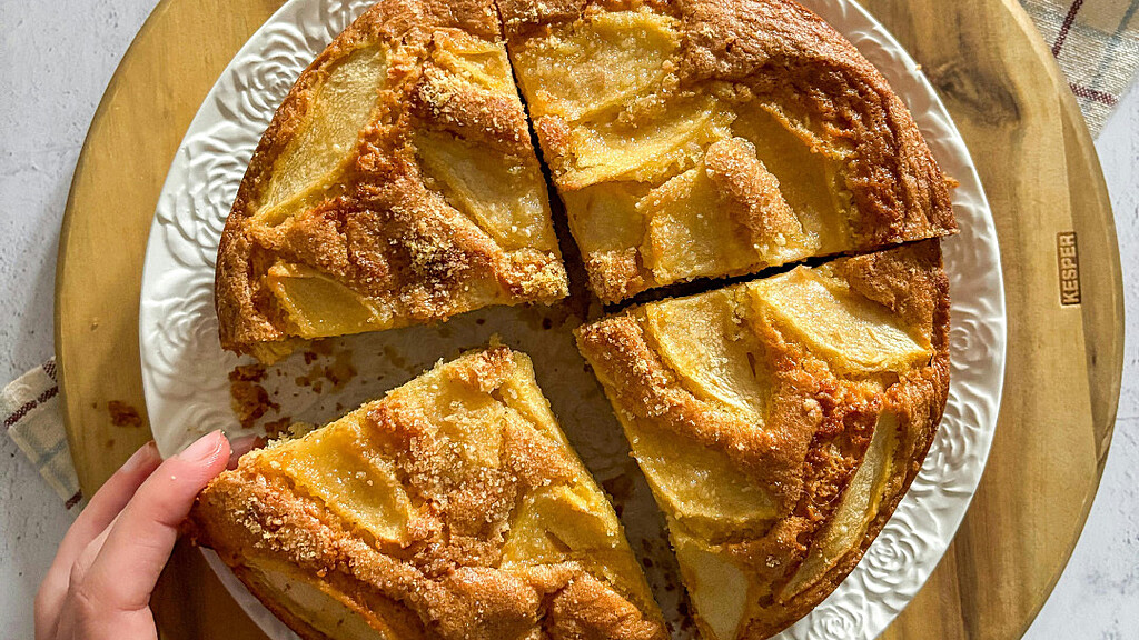 Birds eye view of French Apple cake with a hand reaching for a slice