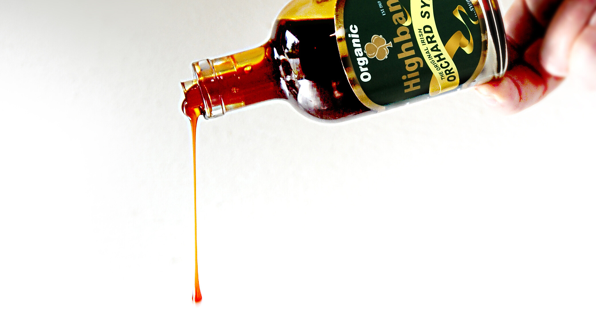 hand held,200ml bottle of orchard syrup, drizzling through the air, on a white background