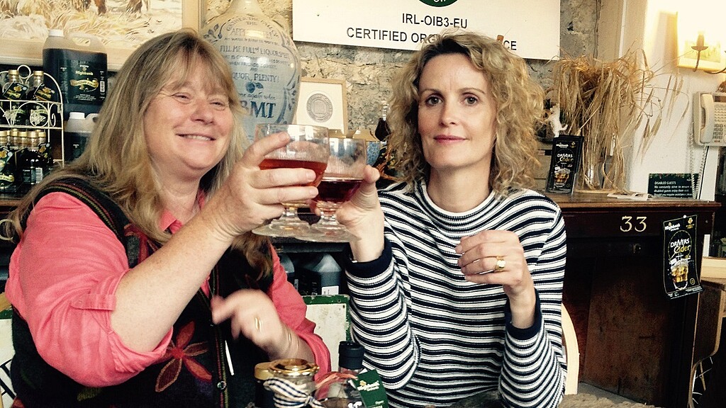 two ladies at a table in the shop clinking glasses with apples in a dish