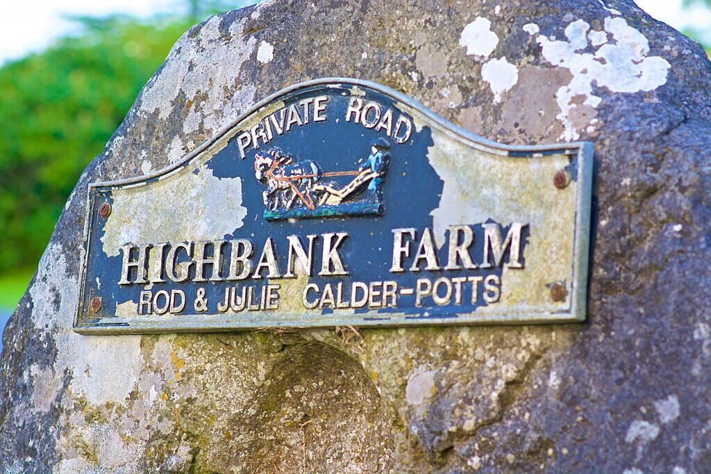 highbank farm cast iron sign with man and plough and private road written on it. The sign is pinned to an old stone mill wheel
