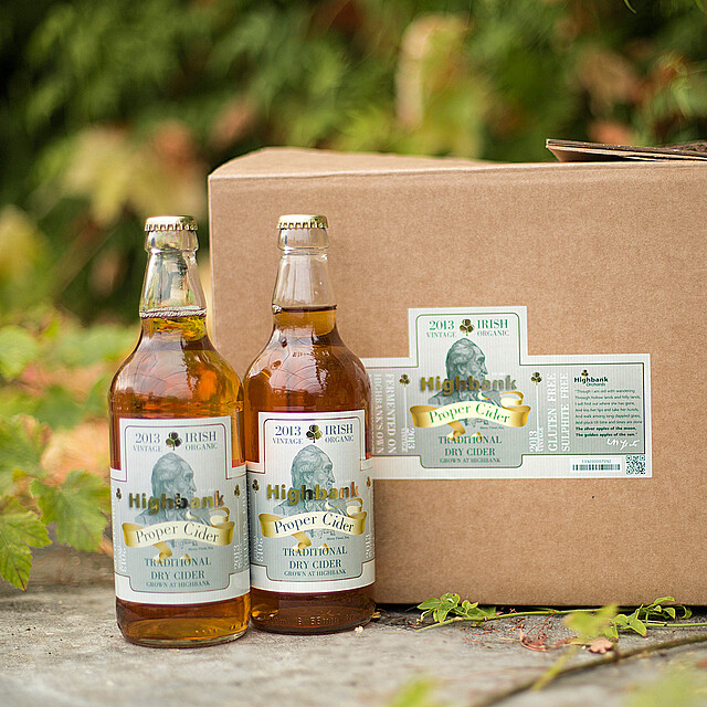 Two bottle of Highbank Proper Cider in front of a case of same in Orchard.