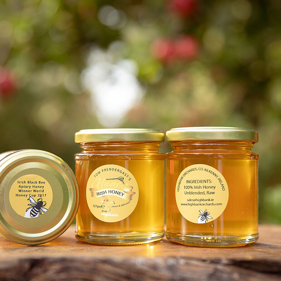 3 x round glass jars of Highbank honey one on its side, on wood in the orchards  The label is circular with a yellow background