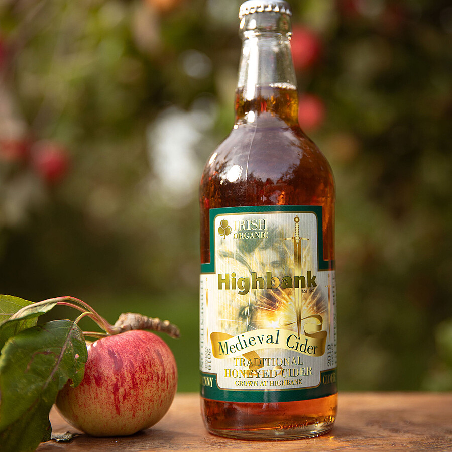 330ml glass bottles of cider in the orchards on wood with a red apple with leaves beside the bottle. The label reads Medieval cider with a picture of a girl and horse,