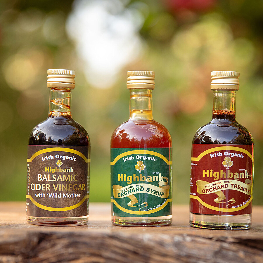 3 x 50ml glass bottles on a piece of wood in the orchards. Highbank Apple Balsamic Vinegar,( brown label) Highbank Orchard Syrup (green label) and Highbank Apple Treacle (red label)