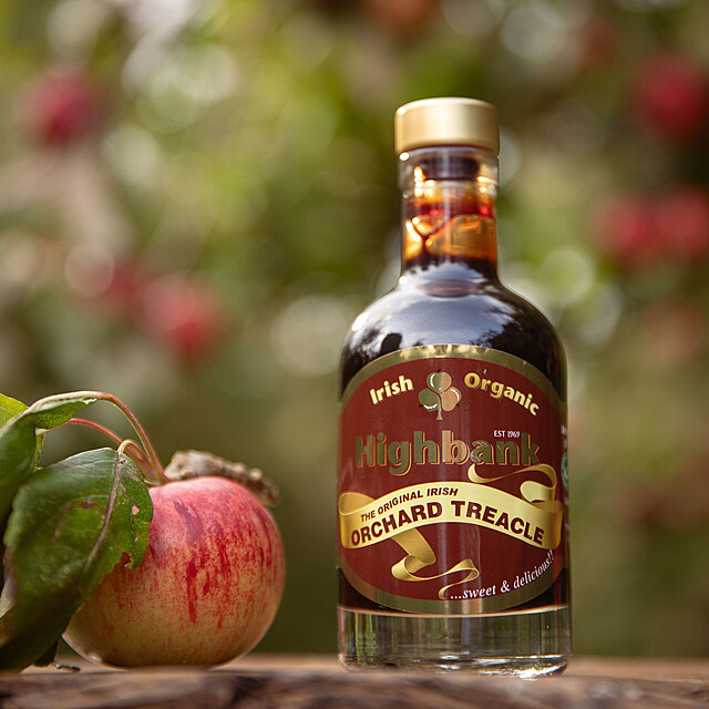 200ml bottle of orchard Treacle on wood beside an apple with leaves. Dark red label with yellow sash