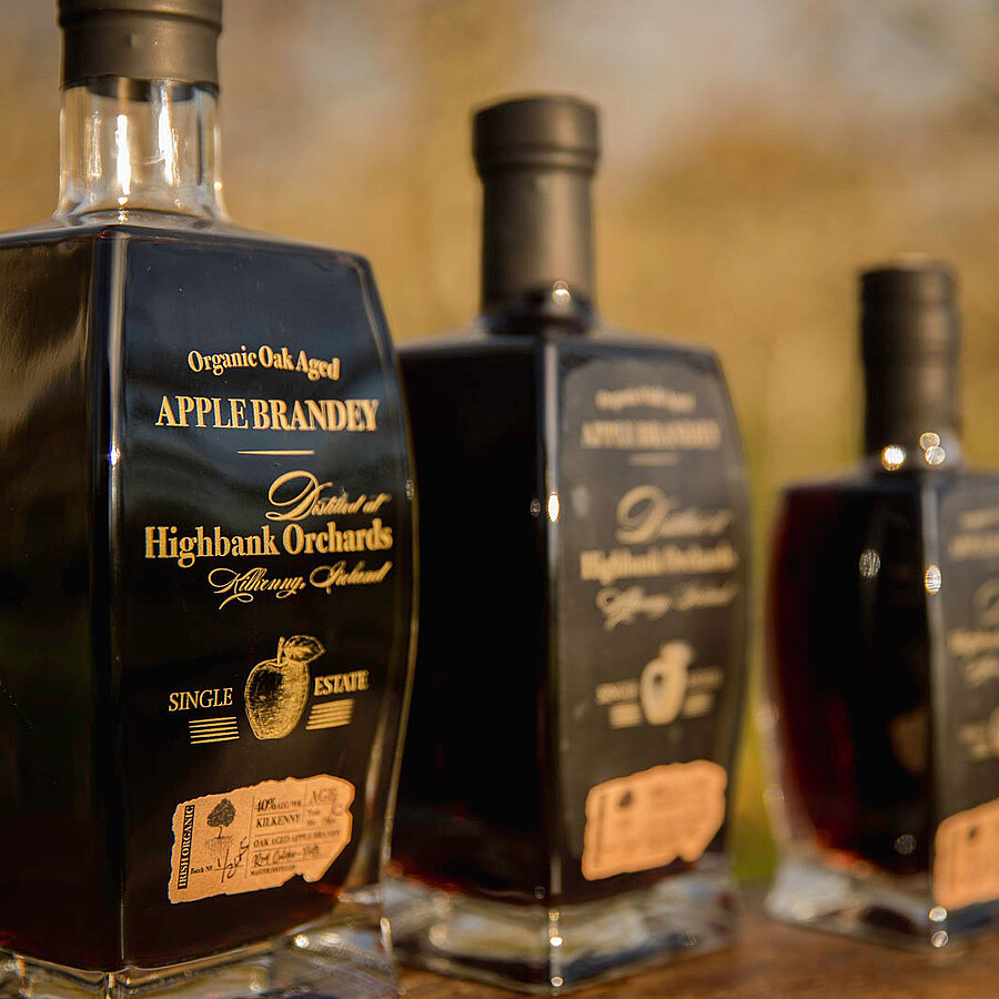 3 square glass bottle of Highbank Organic Apple Brandey in a line in the orchards with brown owner signed labels. 700ml, 500ml and 200ml