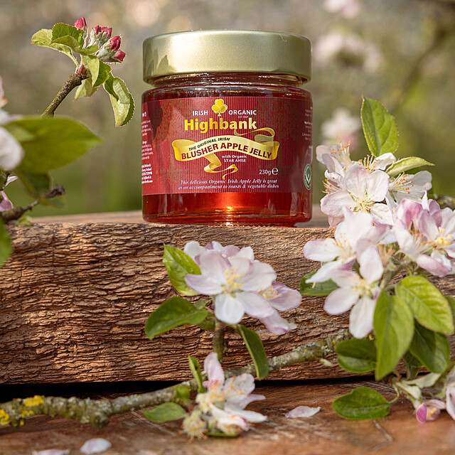 round glass Jar of red apple jelly  with a gold top on wood surrounded by apple blossom