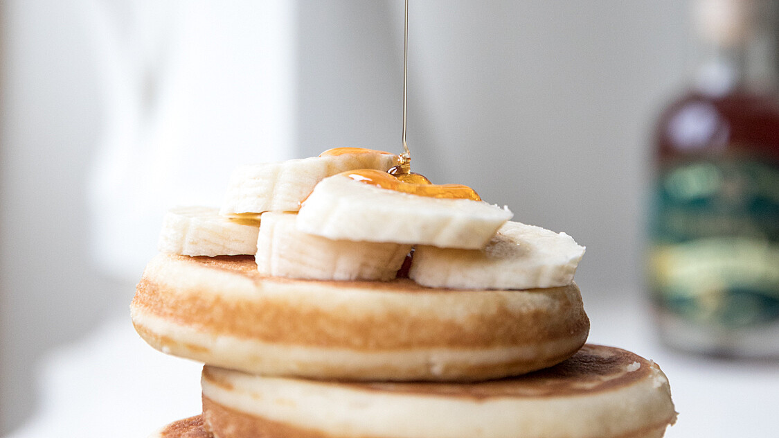 stack of pancakes with Highbank Orchard Syrup being drizzled down on them. White jug in background