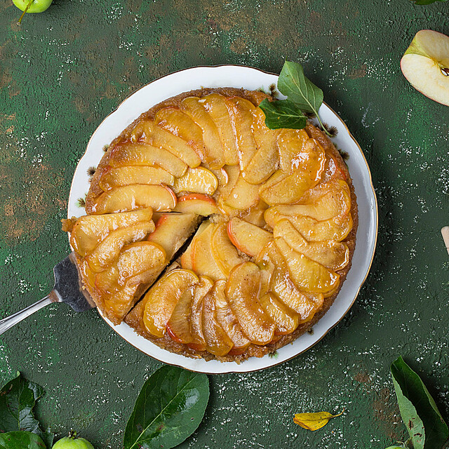 Birds eye view of Blusher apple tart on green table with apples and leaves