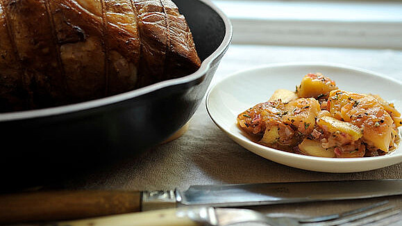 piece of pork in black cooking pot beside white plate of apples