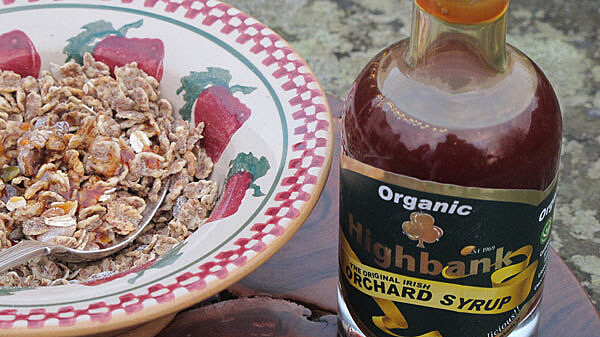 muesli in an apple printed bowl with a bottle of apple syrup beside it.