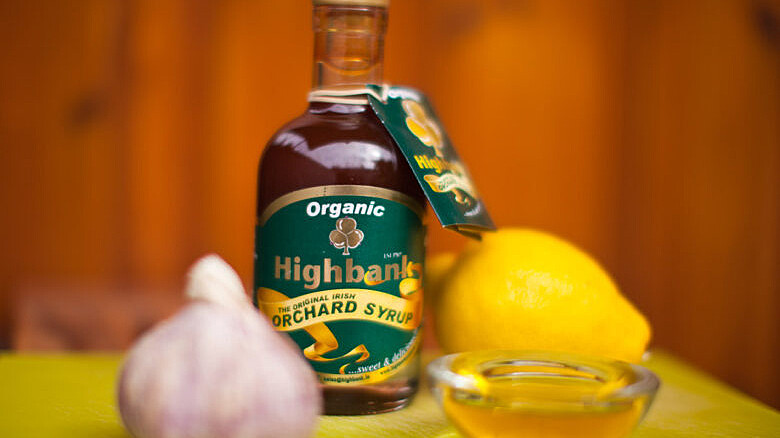 bottle of orchard syrup with a bulb of garlic and lemon beside a dish of olive oil